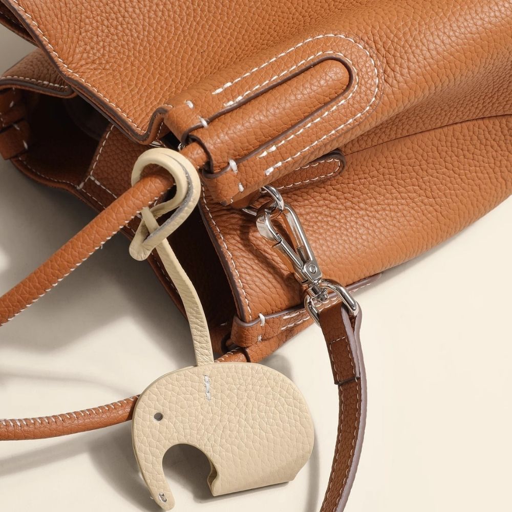 Brown leather bag with a beige elephant-shaped keychain on a light background