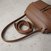 Brown leather handbag with strap on a gray concrete surface