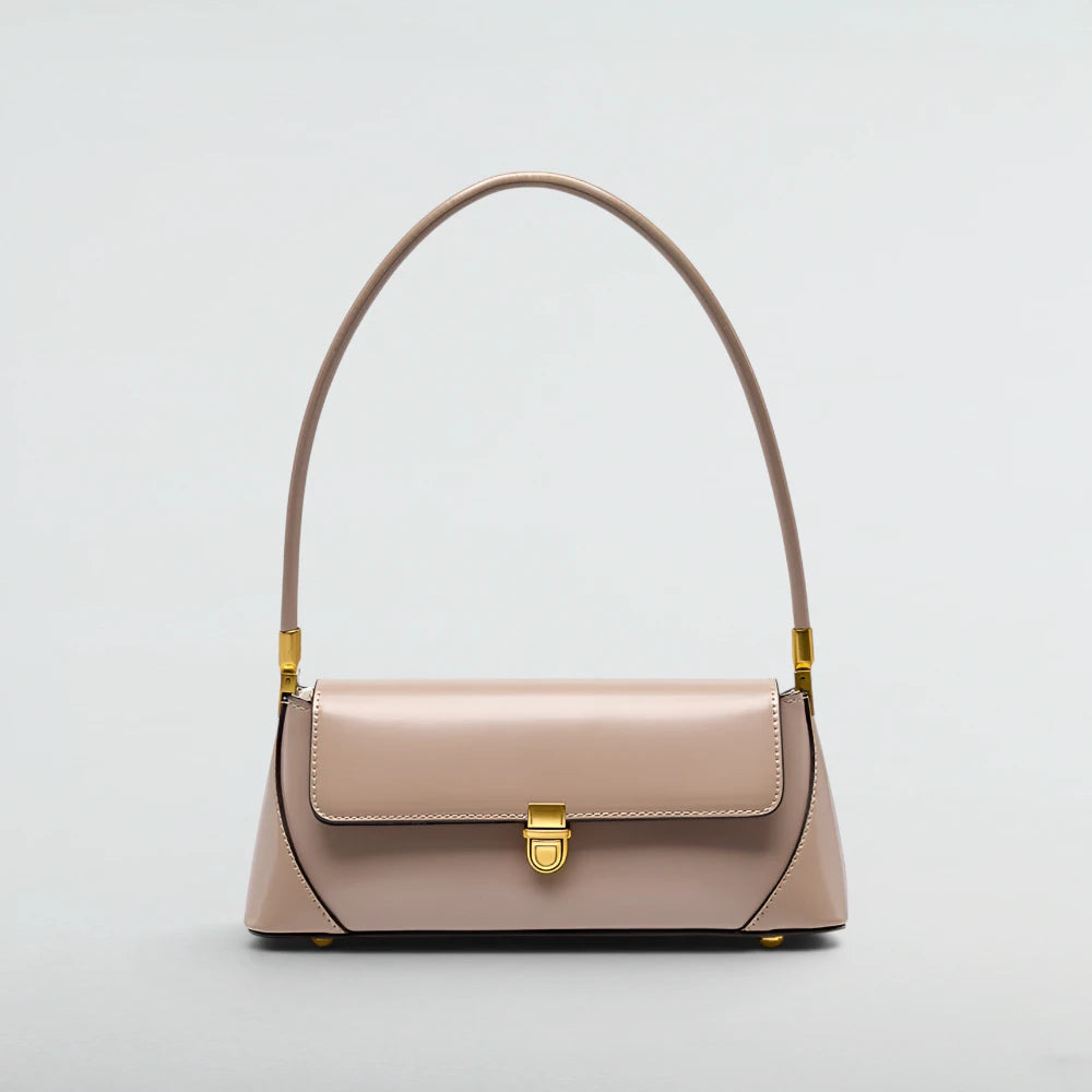 A structured shoulder handbag in a light blush pink leather with gold-tone hardware, featuring a curved top handle and a front flap closure, set against a plain light gray background.