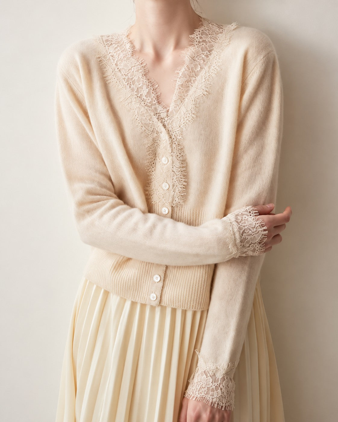Beige lace-trim cardigan with a V neckline, long sleeves and a ribbed waist, worn with a pleated skirt