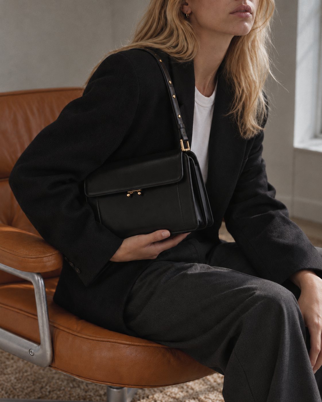 Model wearing the Bagulia Margot leather shoulder bag in black, seated view.