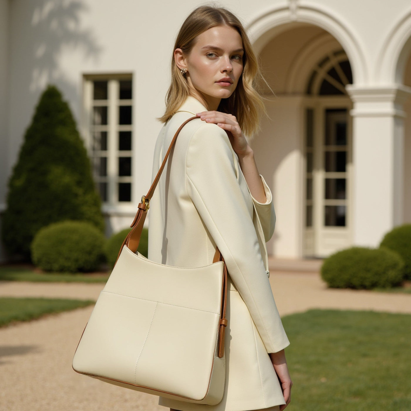 Woman holding a beige handbag in front of a classical building. Bagulia #hero